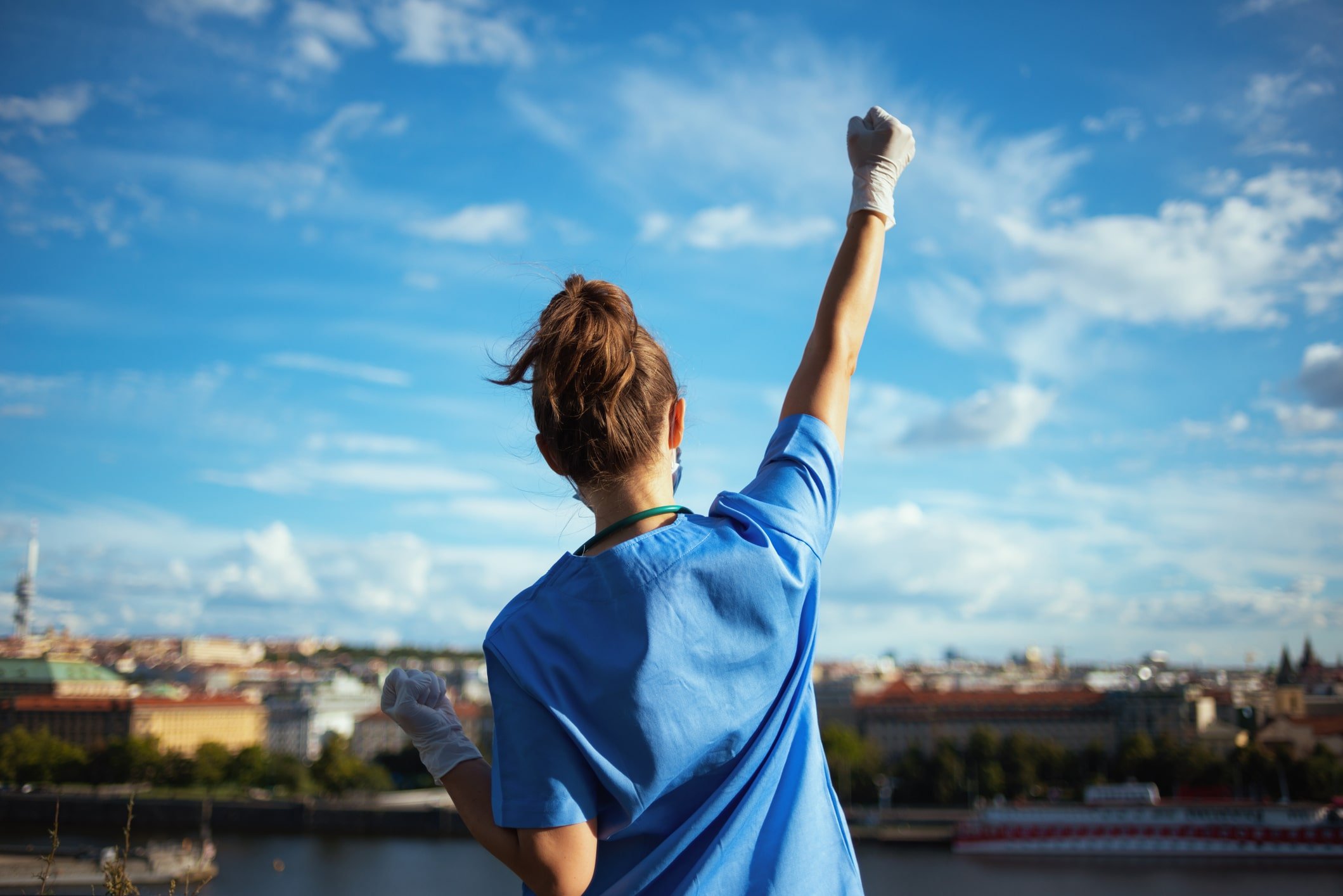 Healthcare professional in blue scrubs raising her arm up to the sky in a celebratory way Healthcare professional in blue scrubs raising her arm up to the sky in a celebratory way