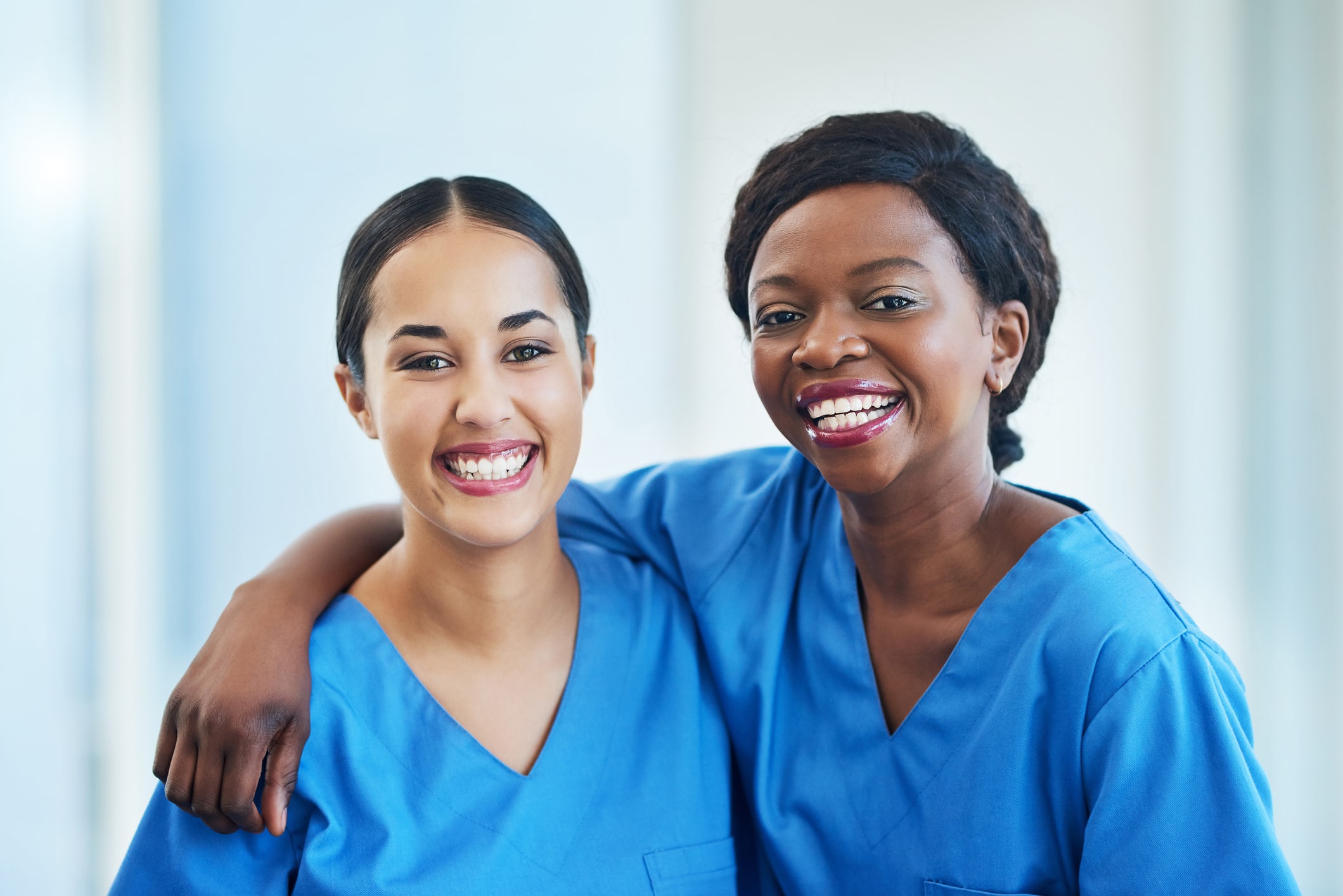 Two female nurses standing next to each other in friendly embrace