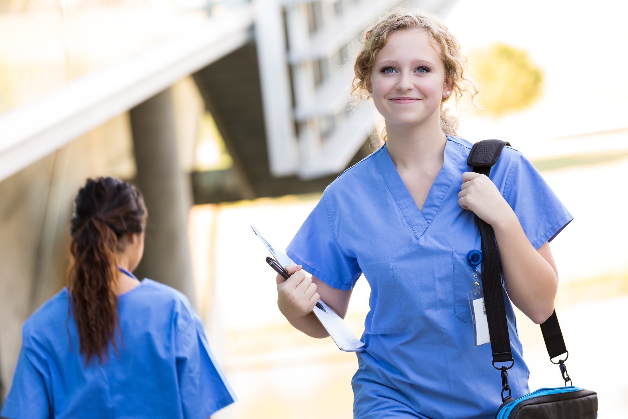 Smiling nursing student in blue scrubs carrying a bag on her shoulder.